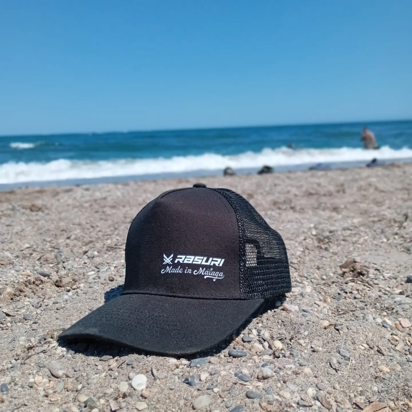 Gorra Rasuri Made in Málaga sobre la arena, junto al mar